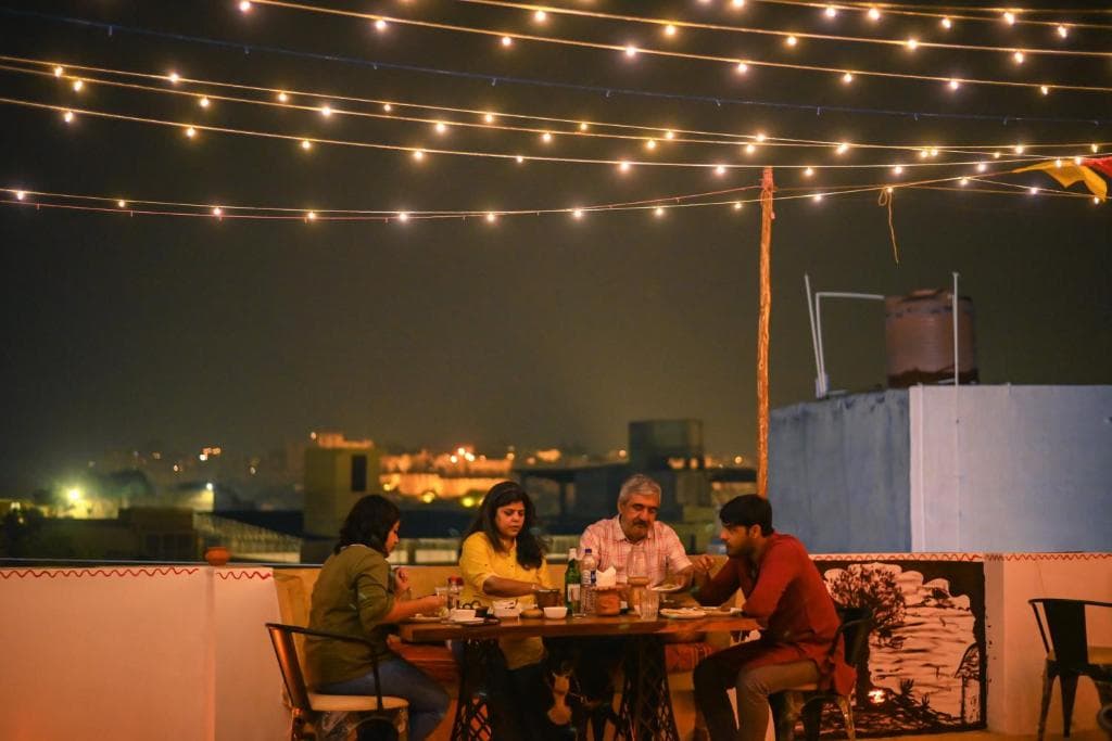 Guests at dinner on the rooftop at night, with Jaisalmer Fort lit up behind