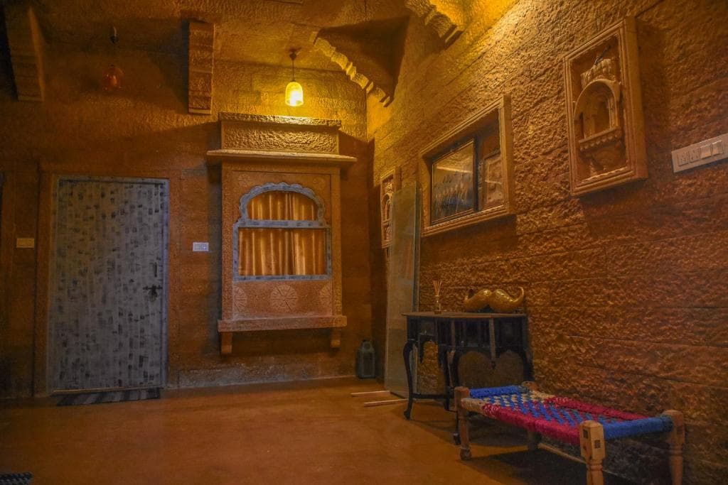 A sandstone corridor with a carved jharokha and a charpai